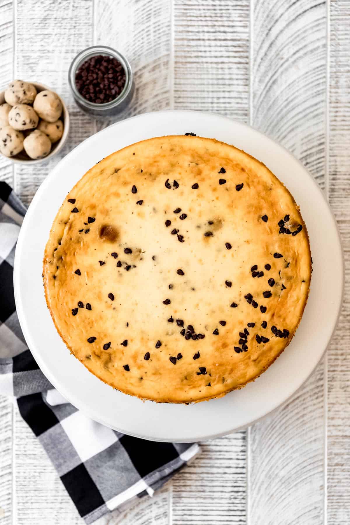 An overhead image of baked chocolate chip cookie dough cheesecake, with a jar of mini chocolate chips and edible cookie dough balls on the side. 