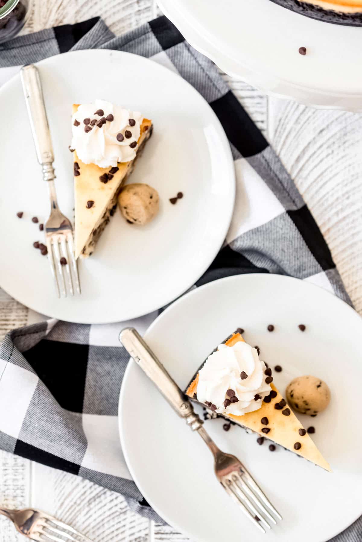 Two slices of cheesecake on plates, with forks and edible cookie dough. 