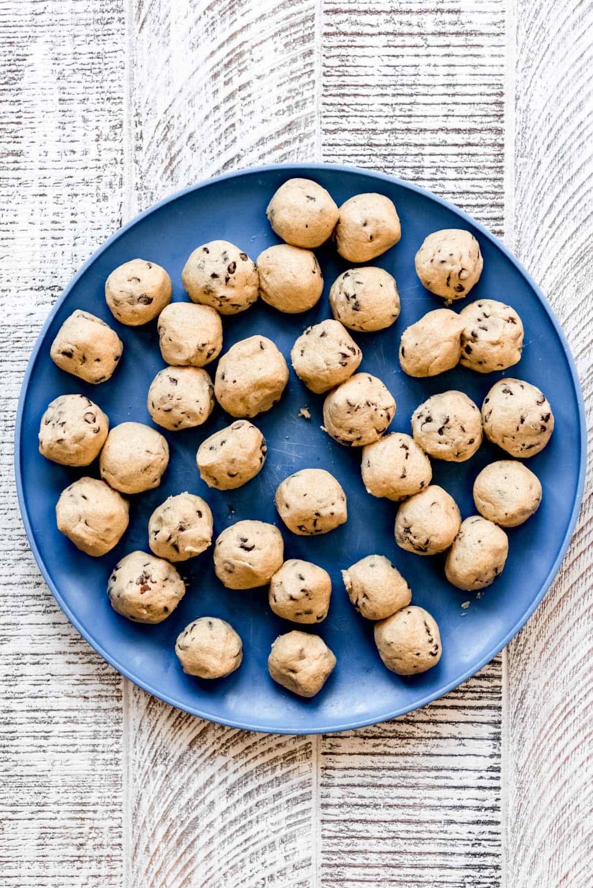 Edible chocolate chip cookie dough is rolled into small balls and displayed on a blue plate. 