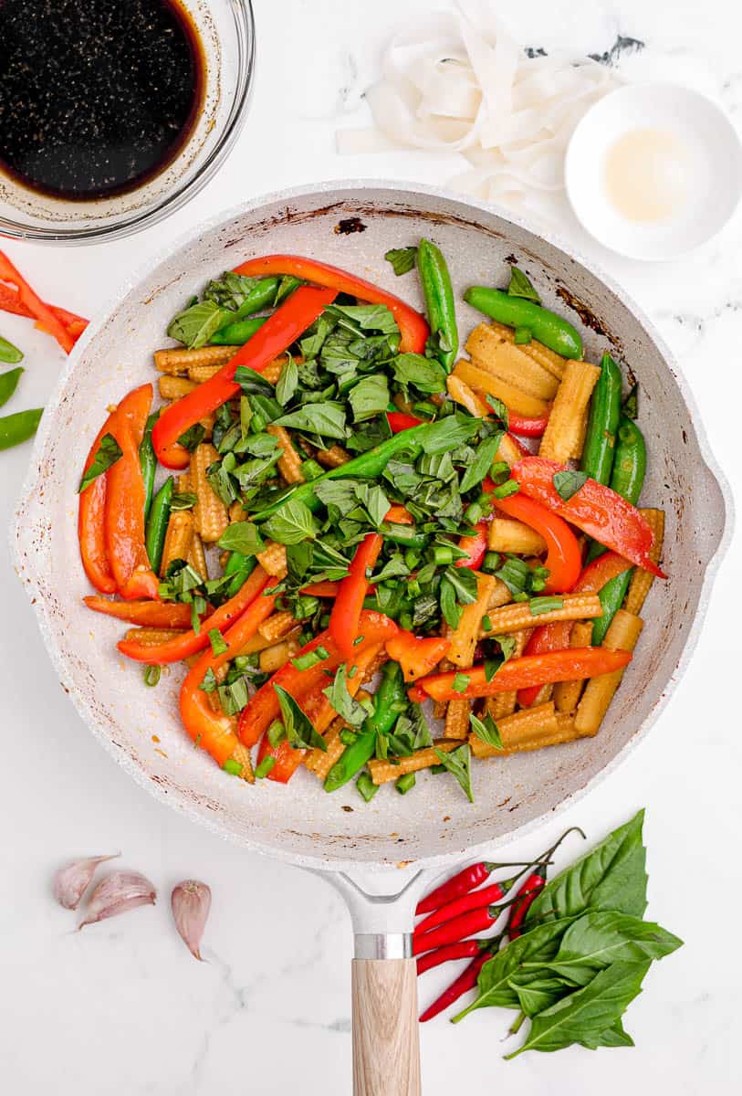 Adding chopped Thai basil to sauteed vegetables in a pan.