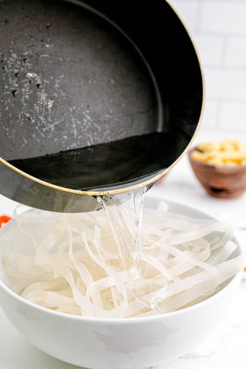 Adding hot water to rice noodles in a bowl.