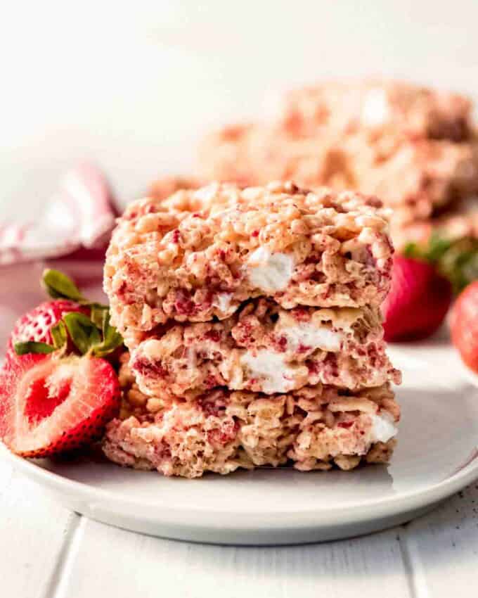 Strawberry Rice Krispies Treats stacked on a white plate served with fresh strawberries.