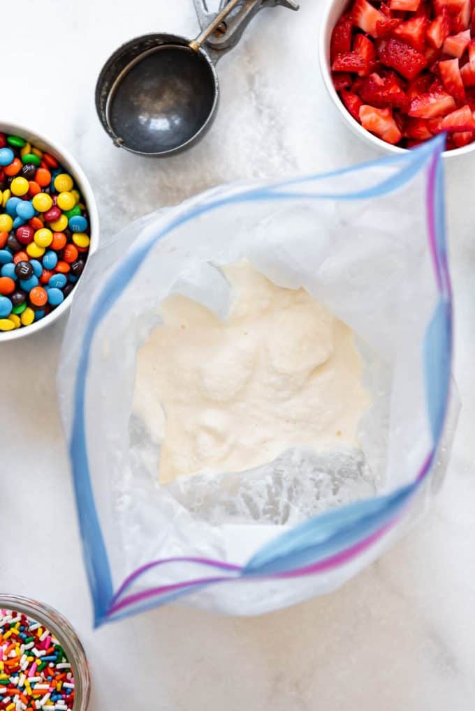 a bag of homemade vanilla ice cream surrounded by bowls of toppings and mix-ins