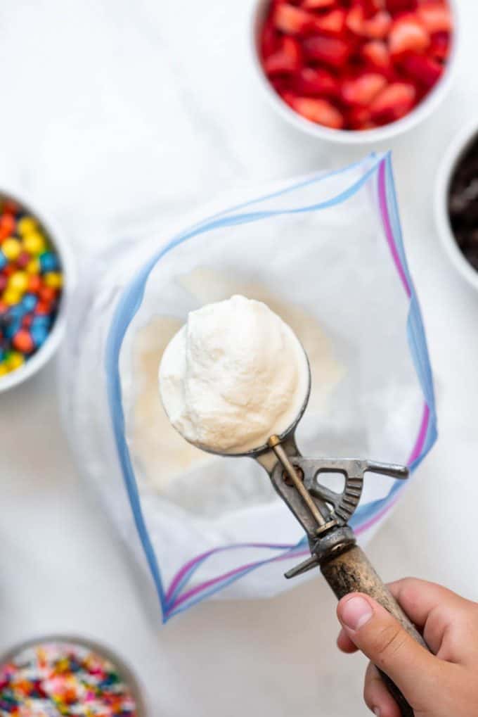 a hand holding a scoop of easy homemade vanilla ice cream made in a bag