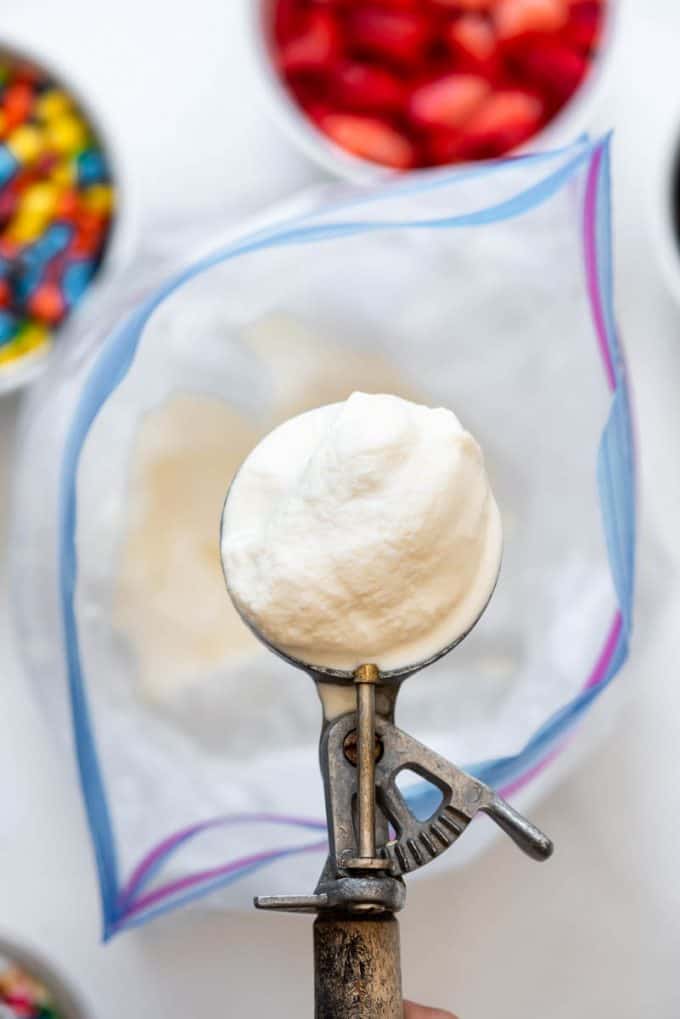 an ice cream scoop holding a scoop of soft serve consistency vanilla ice cream made in a bag with rock salt and ice