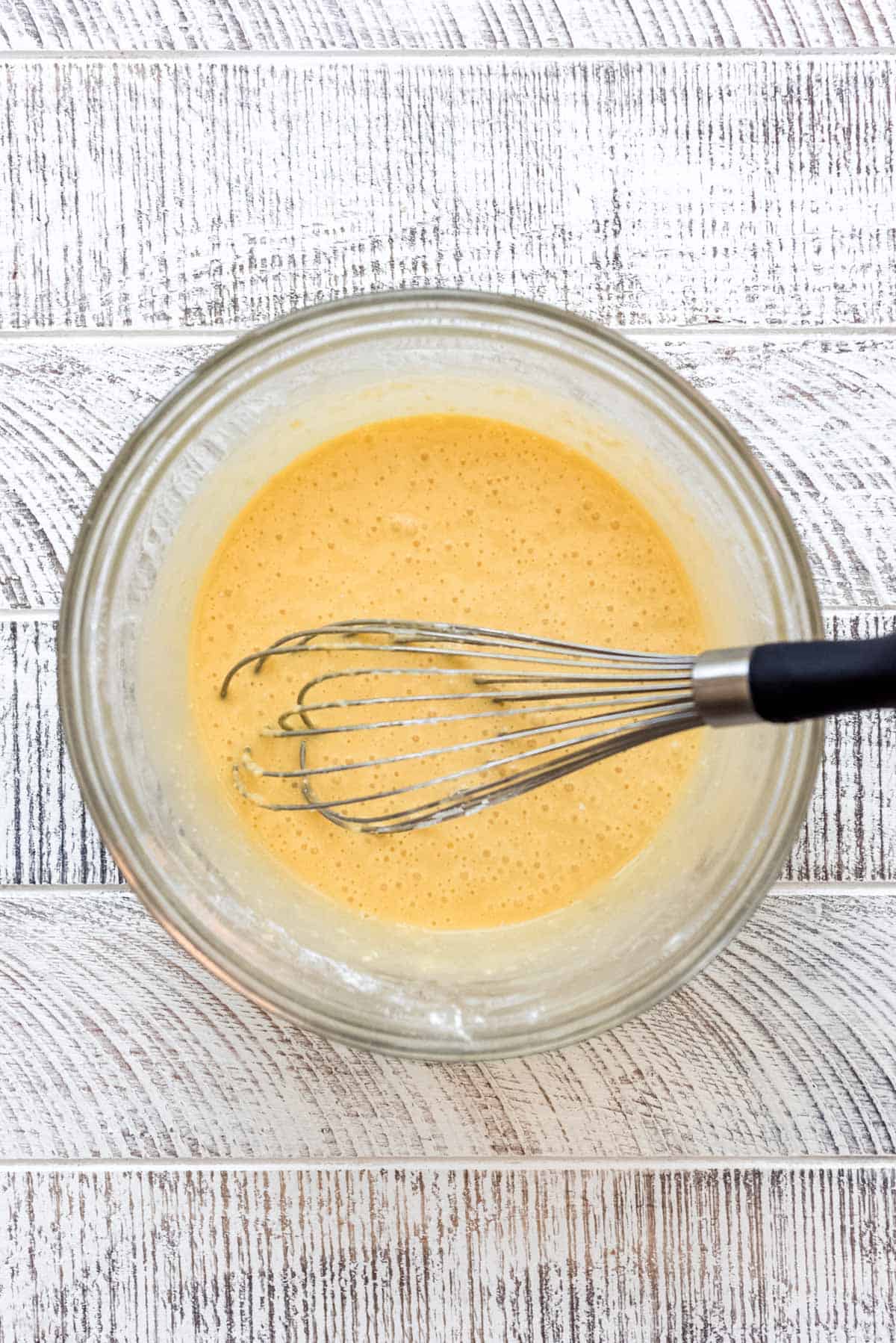 The flour and baking powder are combined with the egg yolk mixture, and the wire whisk is resting in the glass bowl. 