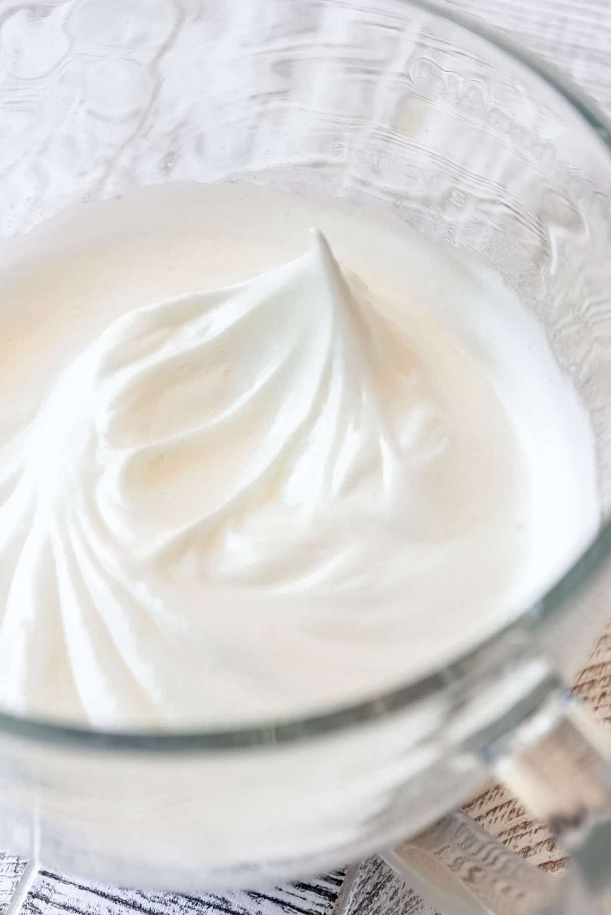 The egg whites have been combined with cream of tartar and sugar, and stiff peaks are visible in the clear glass bowl. 