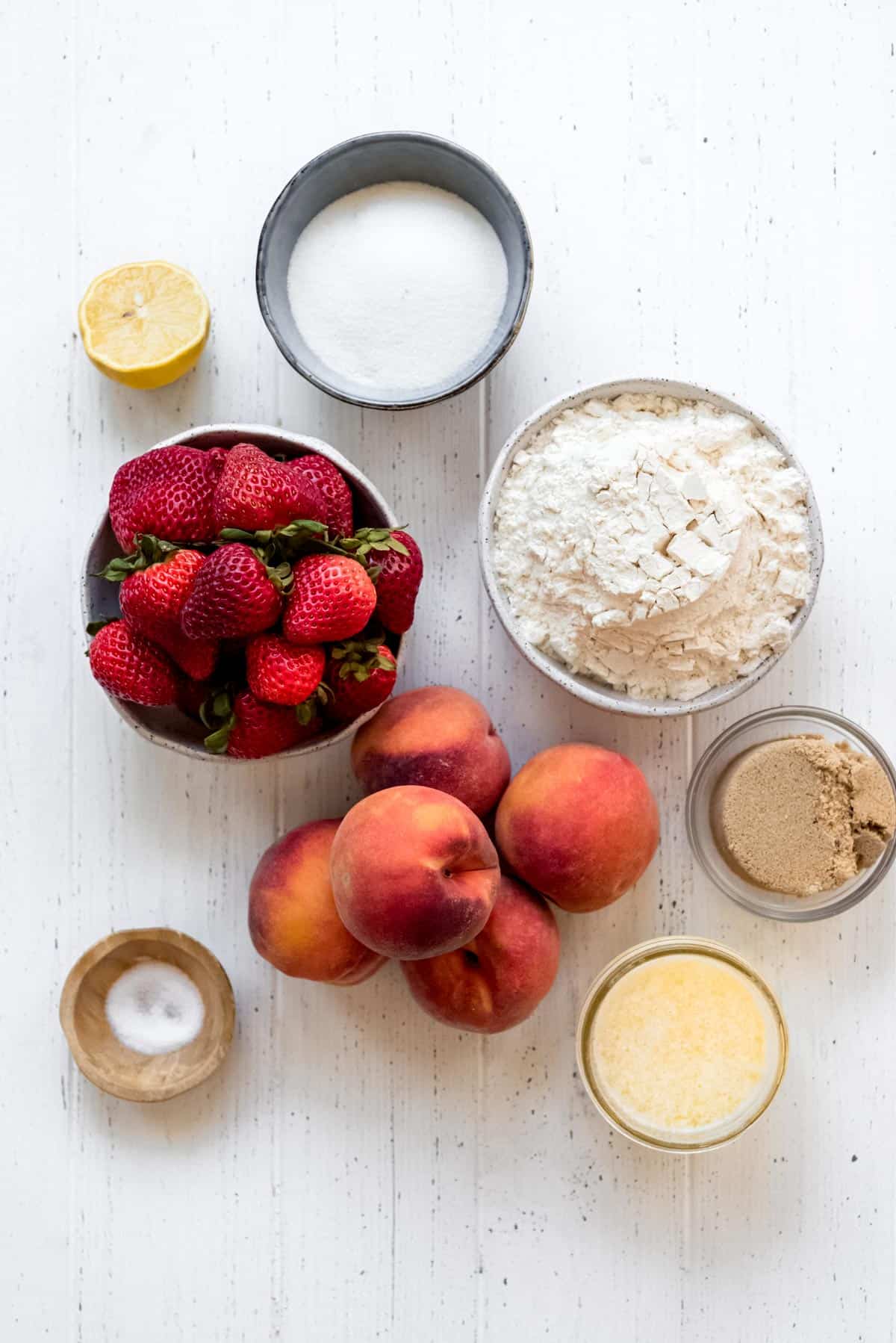 ingredients for a strawberry peach crumble on a white surface