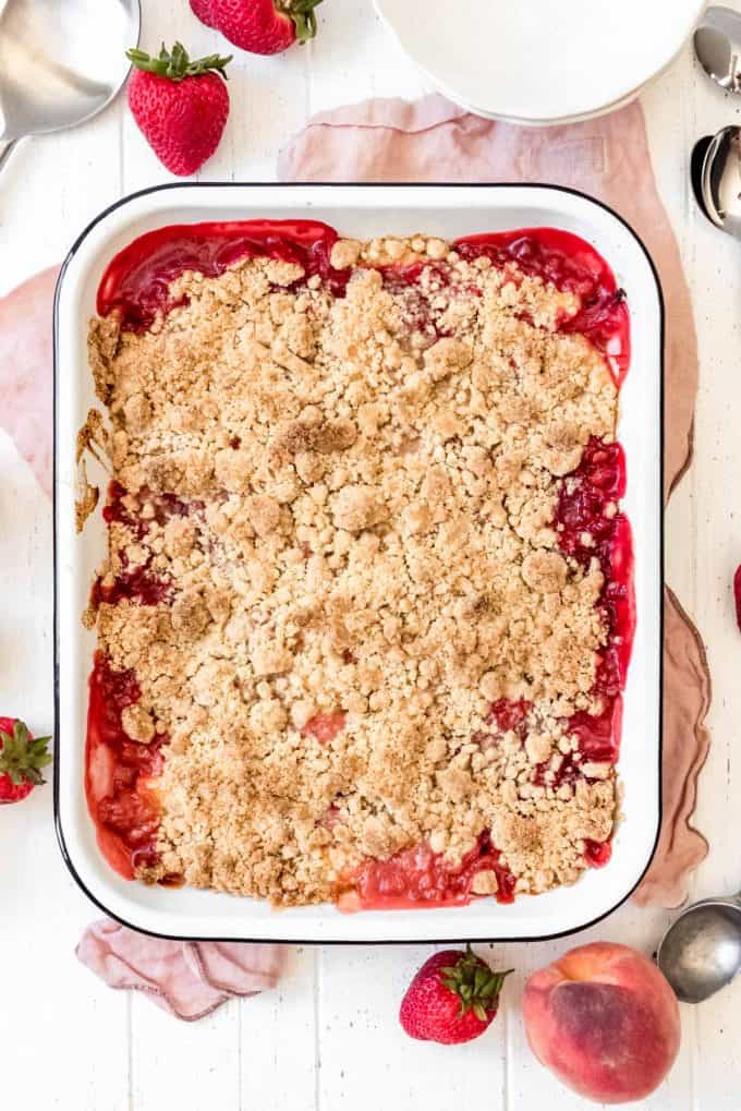 a white enamel baking dish filled with juicy cooked strawberries and peaches with streusel topping