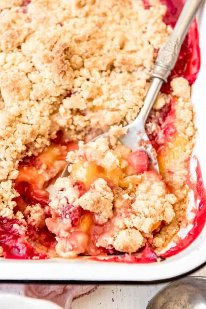a large serving spoon scooping cooked peaches and strawberries with crumble topping