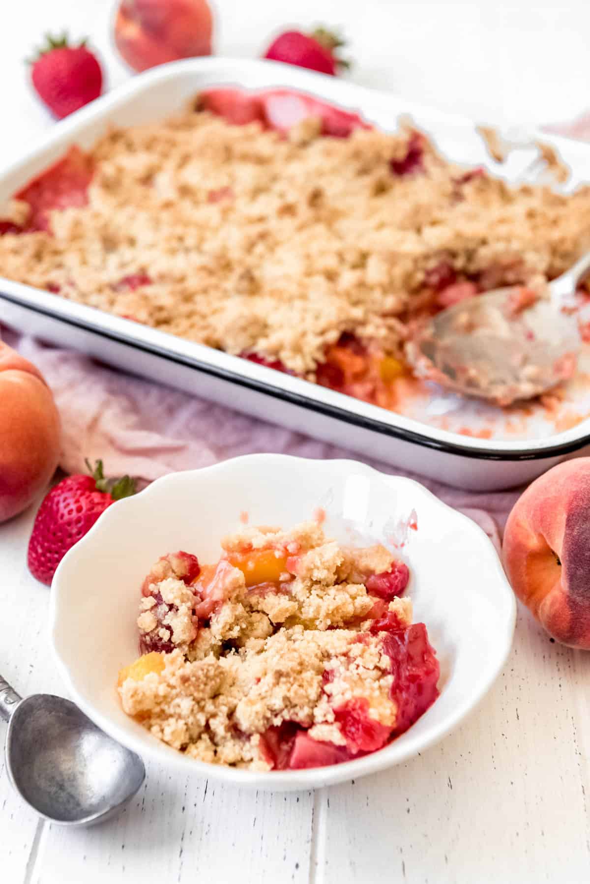 a scoop of strawberry peach crumble in a bowl in front of a baking dish