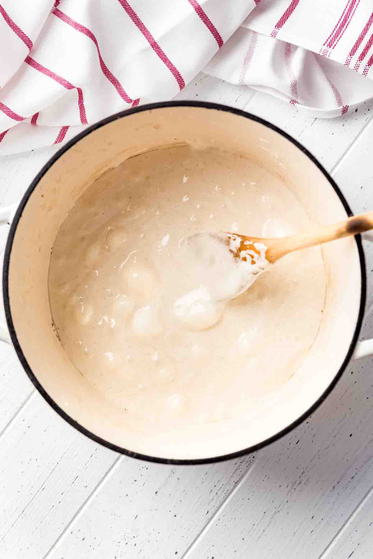 Melted marshmallows are in a large heavy duty pot, with a wooden spoon resting on the side.