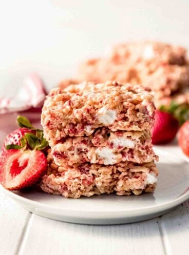 Strawberry Rice Krispies Treats stacked on a white plate served with fresh strawberries.