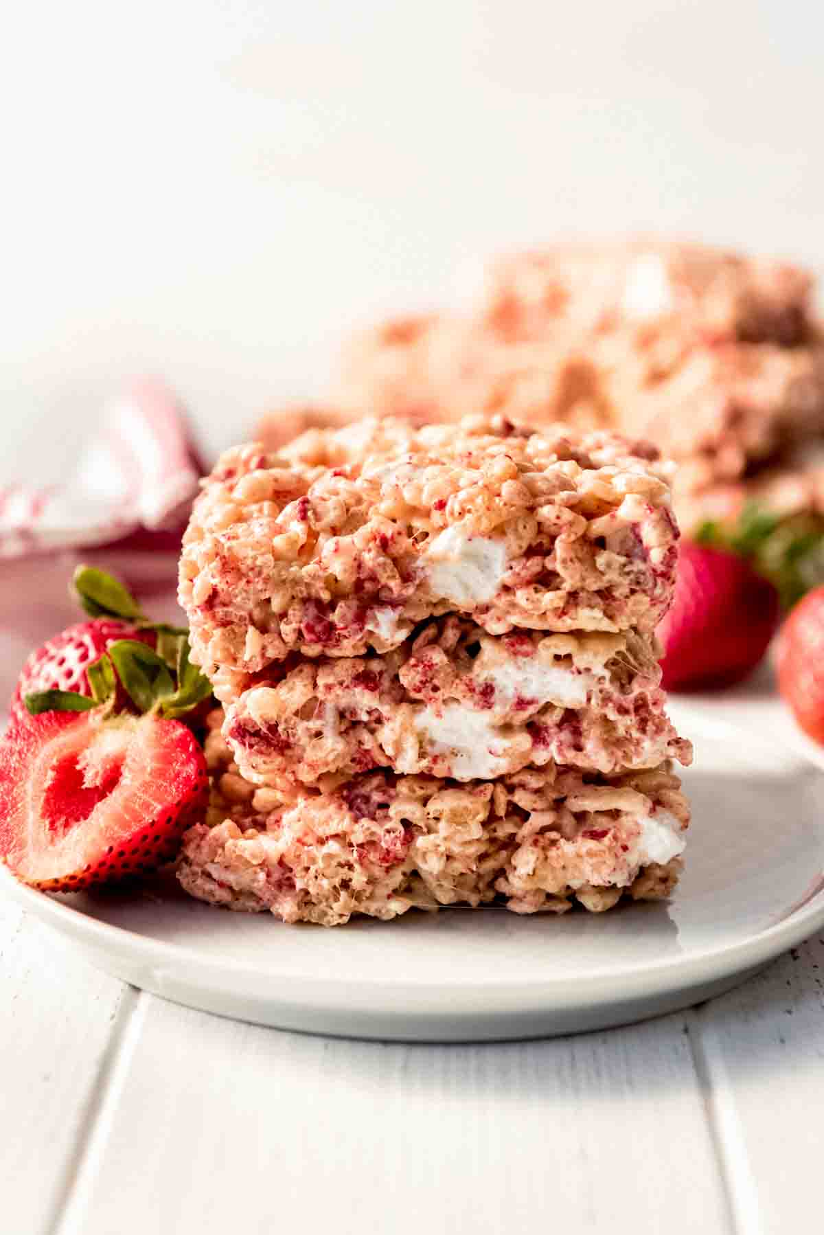 Strawberry Rice Krispies Treats stacked on a white plate served with fresh strawberries.