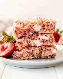 A stack of 3 strawberry rice krispies treats with a fresh strawberry on a white plate