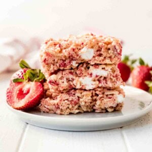 A stack of 3 strawberry rice krispies treats with a fresh strawberry on a white plate