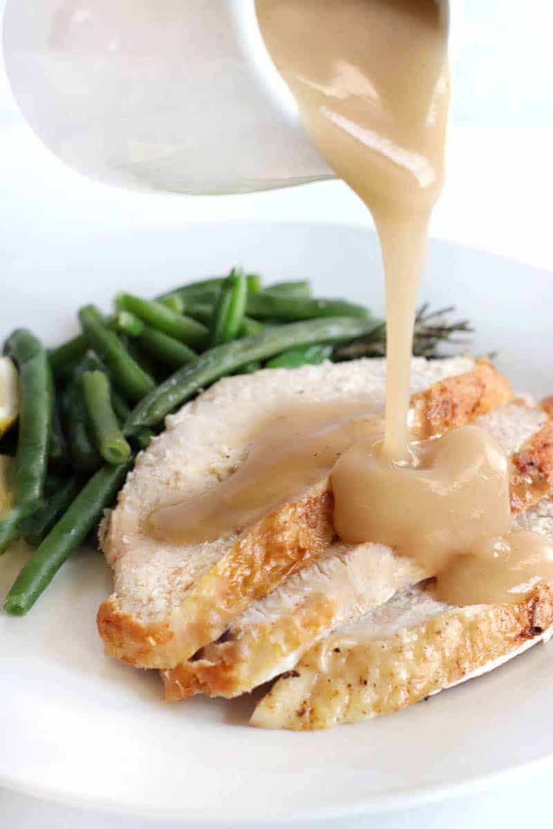 Sliced turkey breast topped with gravy and a side of green beans on a white plate