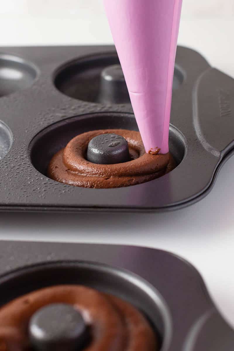 a piping bag filled with chocolate donut batter filling a donut pan