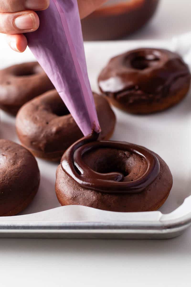 Chocolate glaze is piped onto donuts in a circular pattern. 