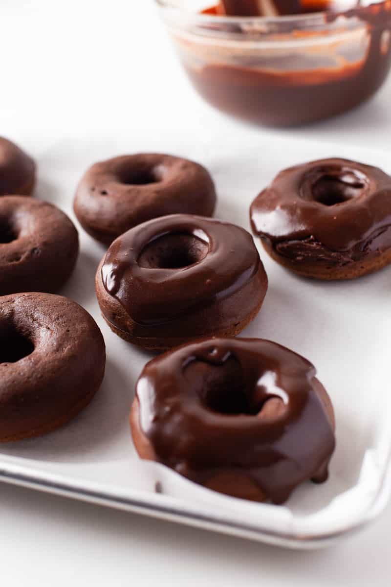 A plate of glazed and unglazed donuts are displayed, with a bowl of chocolate glaze visible in the background. 