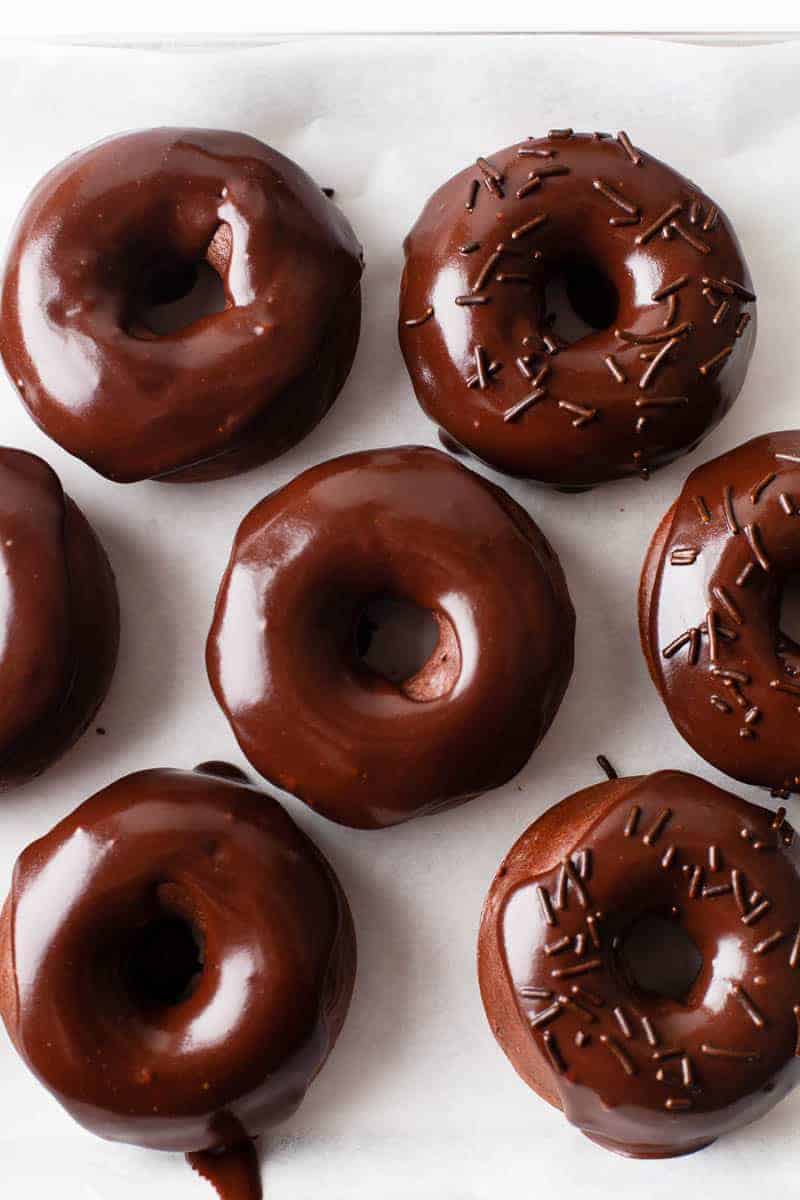 Baked chocolate donuts on a white table with chocolate glaze