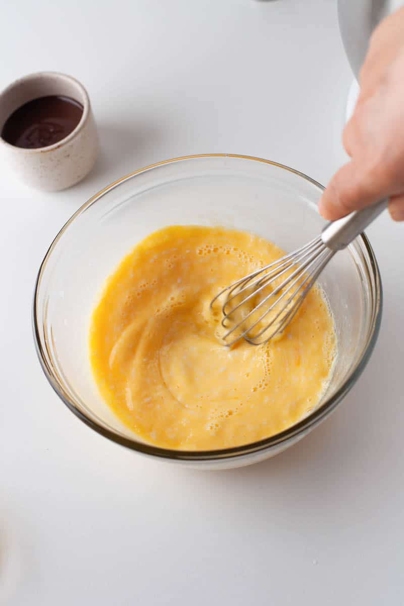 An egg and milk mixture is stirred with a wire whisk.