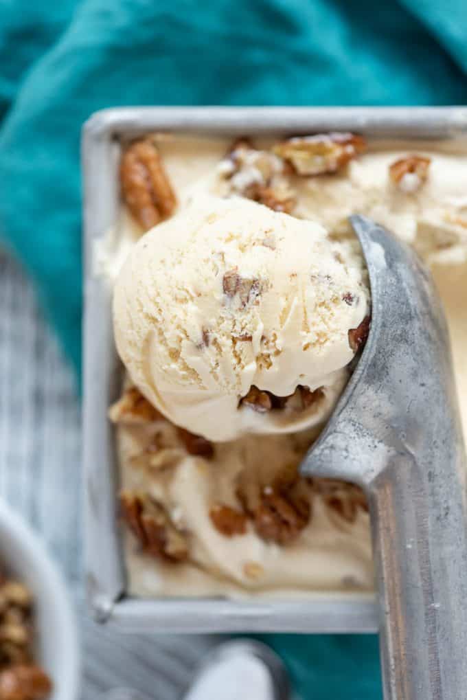 a close image of a scoop of butter pecan ice cream and a metal ice cream scooper