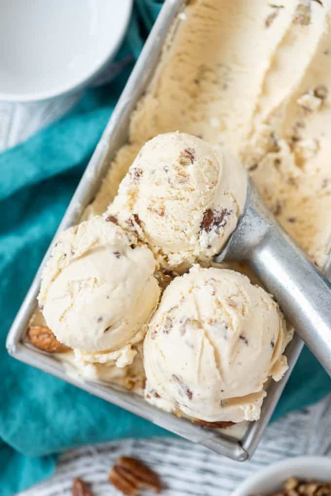 three scoops of homemade butter pecan ice cream on top of the container of ice cream