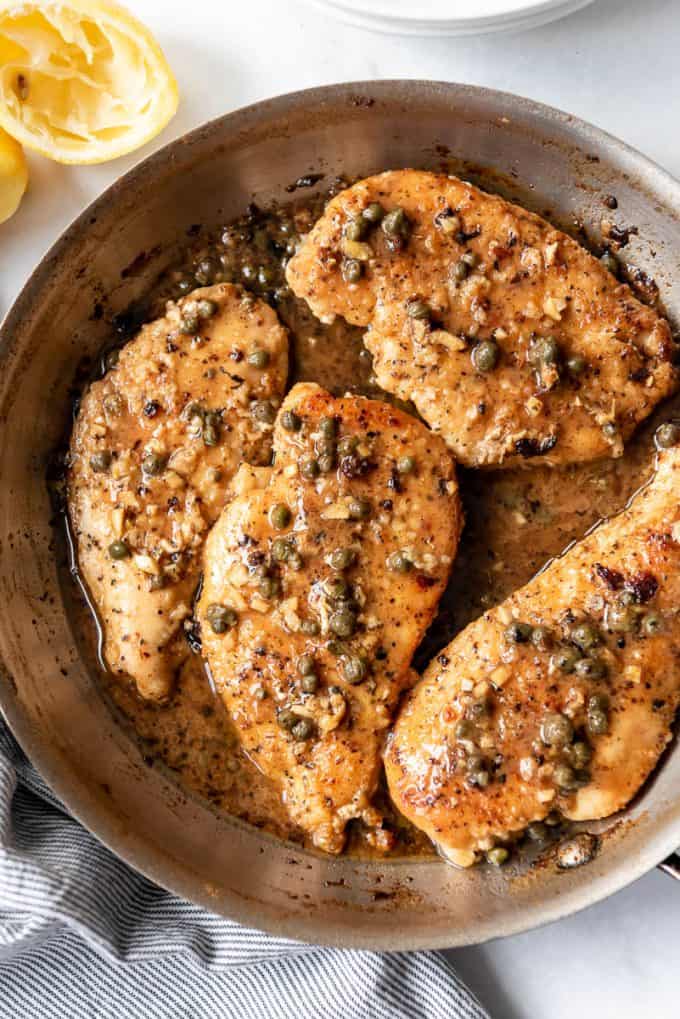 chicken breasts in a pan with a lemon caper pan sauce for chicken piccata
