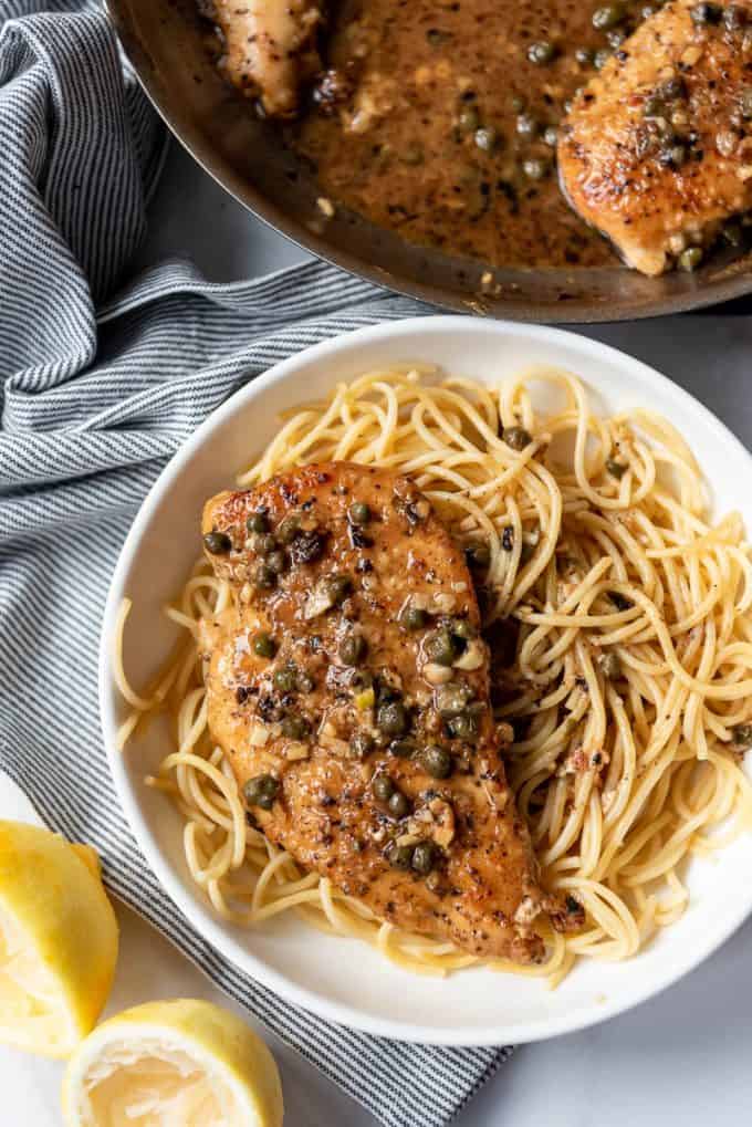 chicken piccata over a bed of pasta in a white pasta bowl