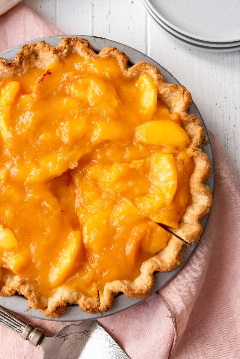 a peach pie with two slices cut into it on a pink linen napkin