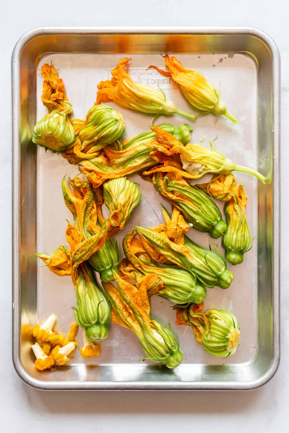 An image of stuffed squash blossoms on a baking sheet.