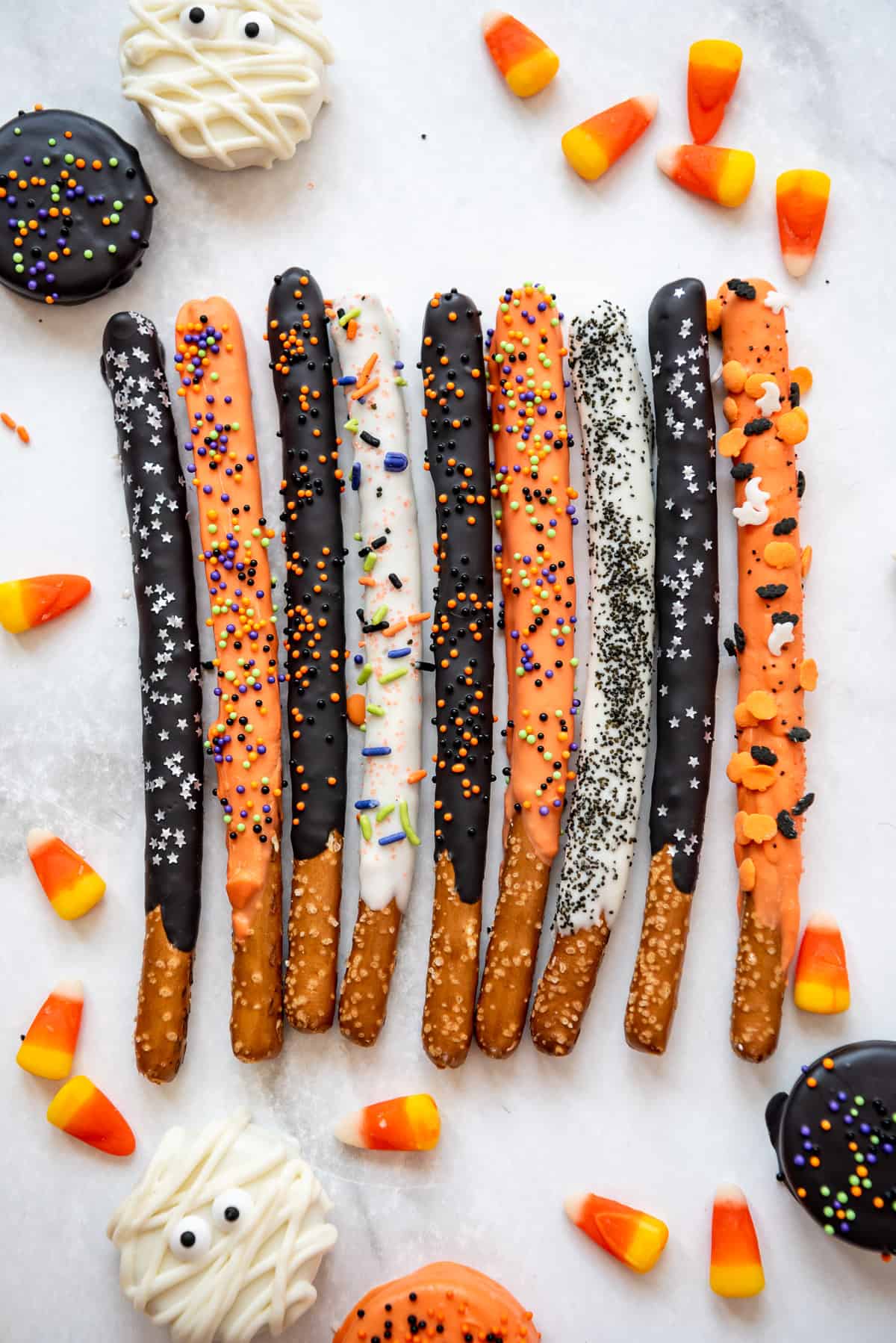 Halloween pretzels decorated with black, white, and orange melted chocolate and sprinkles.