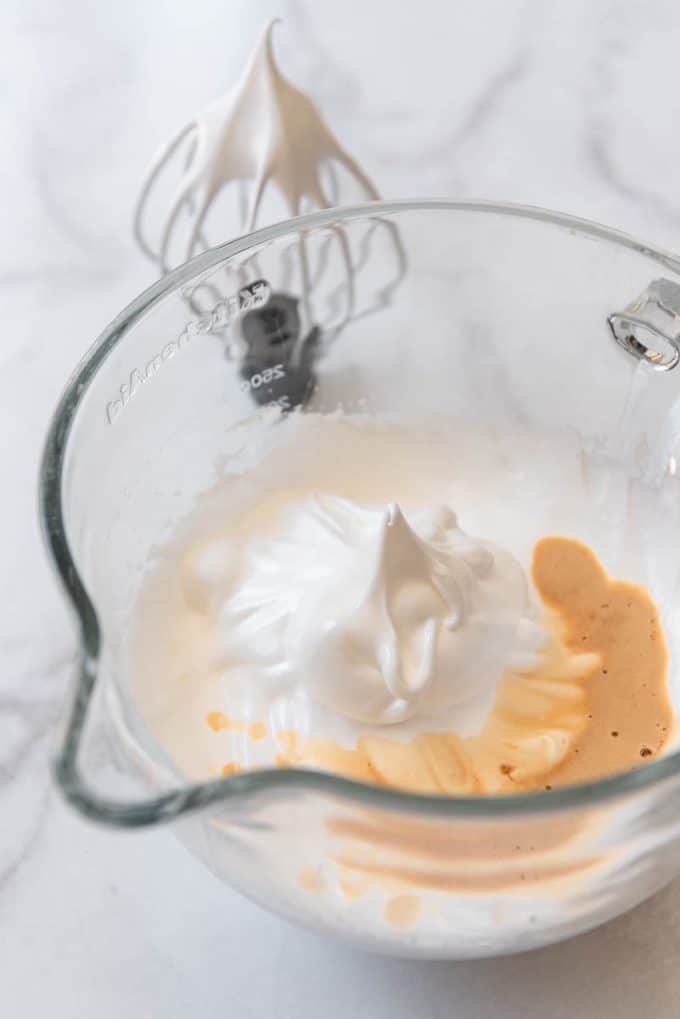 Egg whites beaten to stiff peaks in a bowl with a whisk attachment.