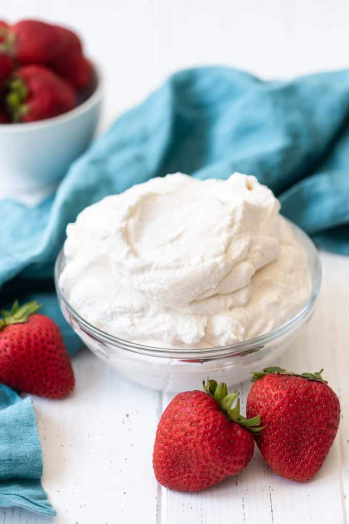 a glass bowl of whipped cream with strawberries beside it