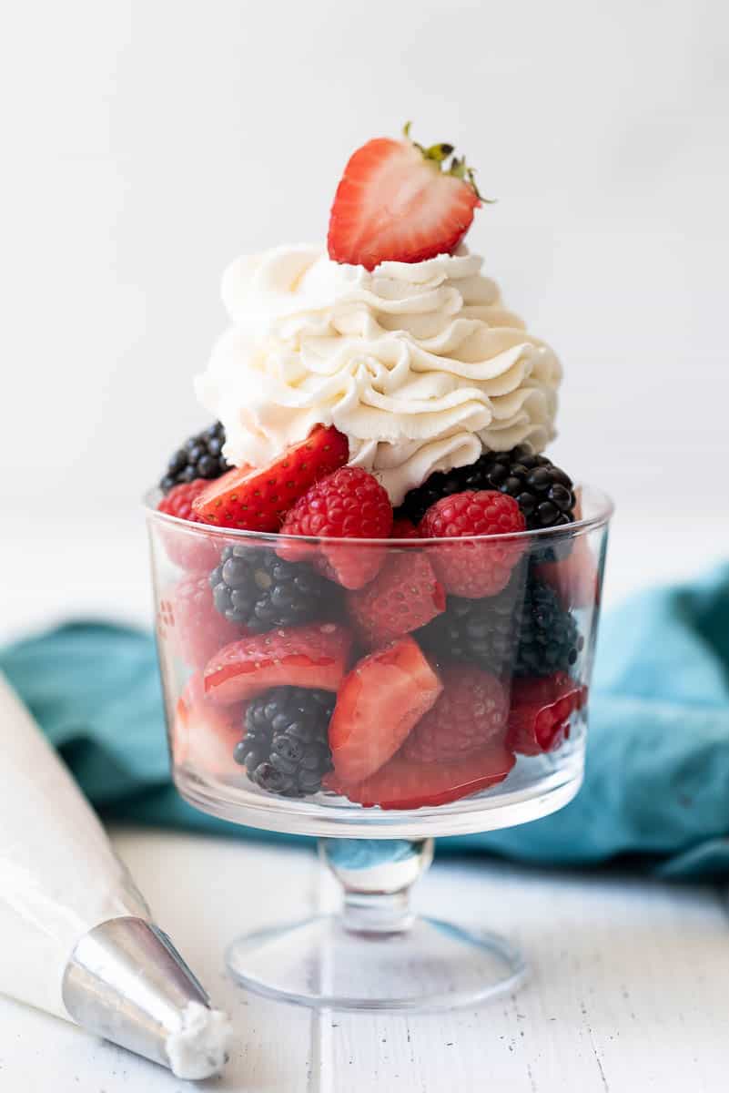 a glass dessert cup filled with fresh berries and whipped cream