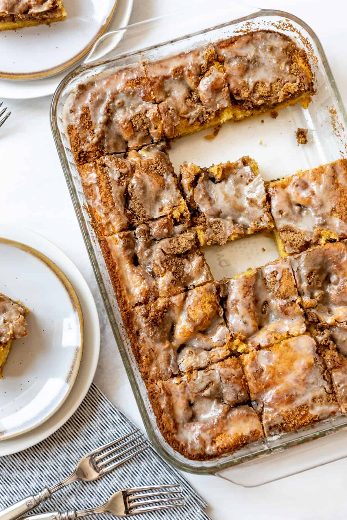 An overhead view of cut honey bun cake in a glass baking dish. Two slices have been removed and plated, visible at the edges of the image. 