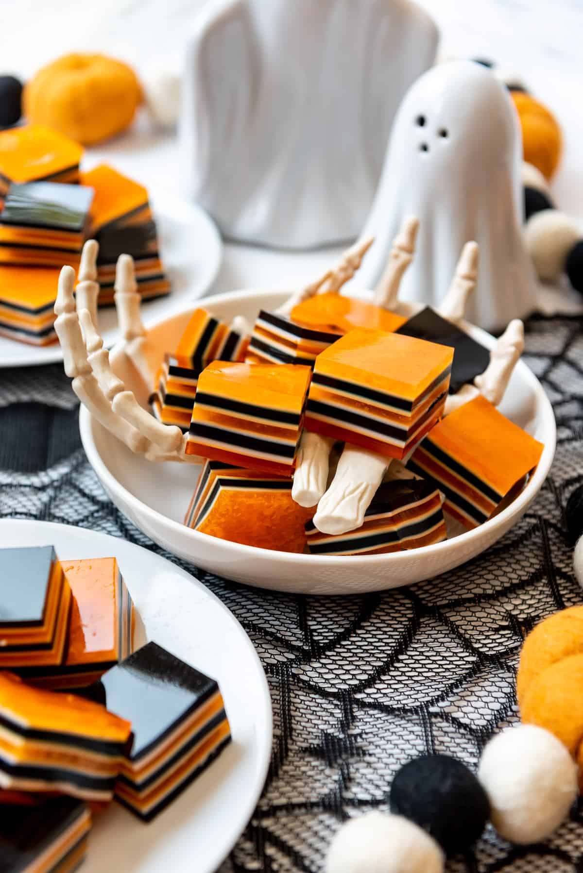 Layered cubes of orange and black jello in a bowl surrounded by Halloween decorations.