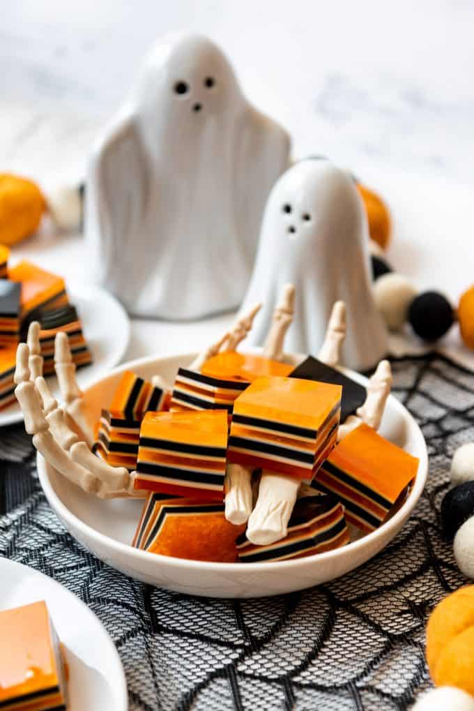 Striped orange, black, and white jello in a bowl surrounded by Halloween decorations.