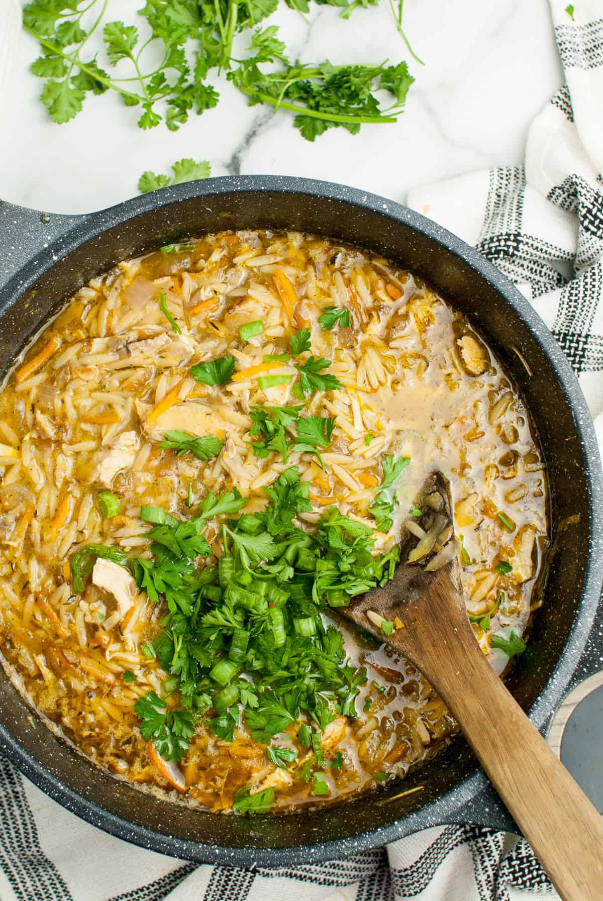 A dutch oven filled with Lemon Chicken Orzo Soup topped with green onion and parsley.