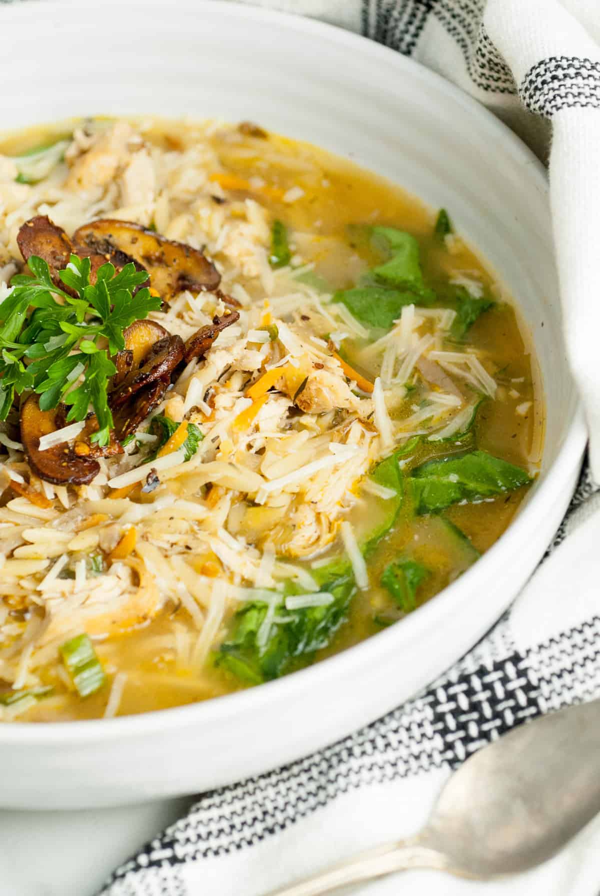 Lemon chicken orzo soup in a white bowl topped with parsley and fried mushrooms.