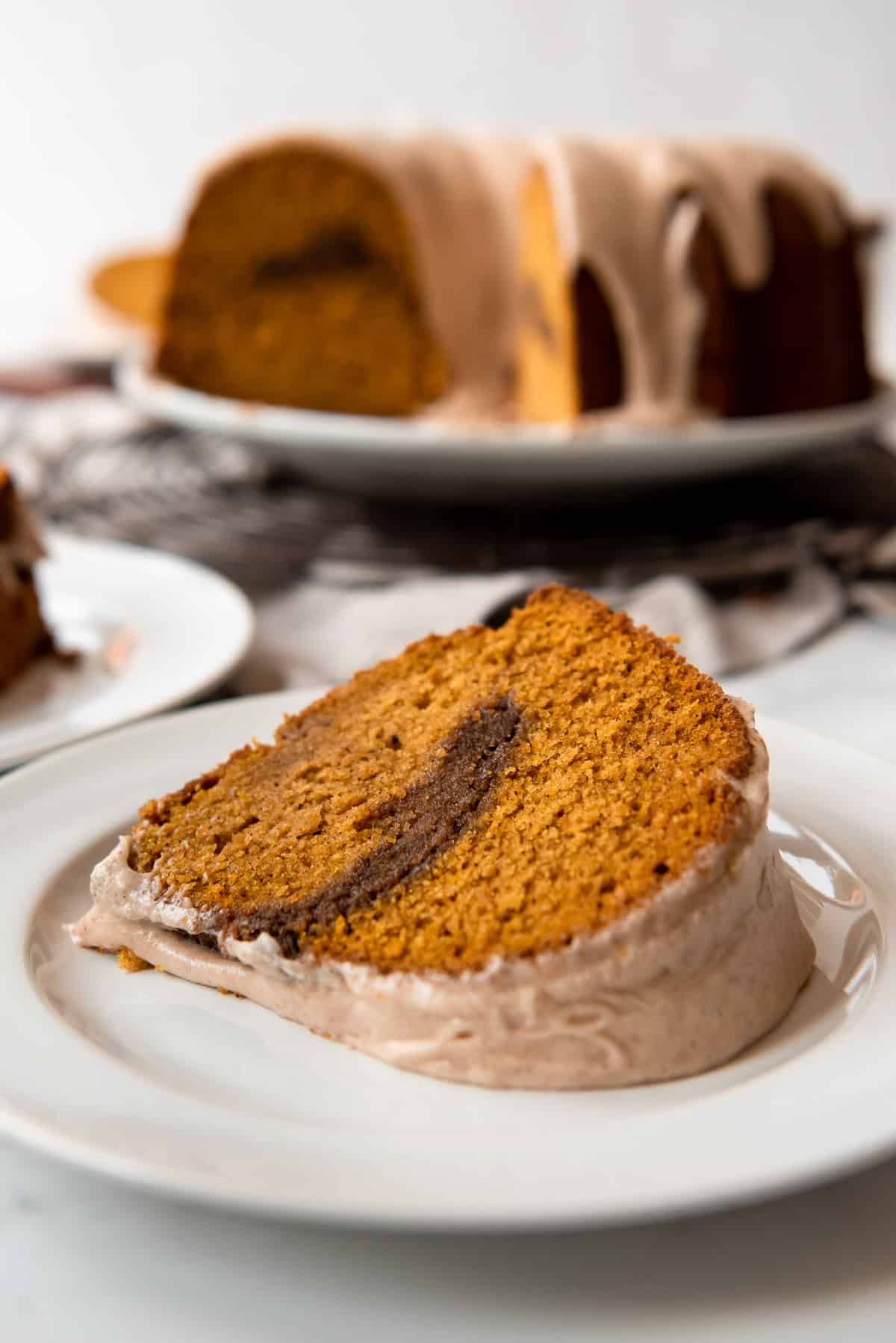 Close up of a single slice of spiced pumpkin bundt cake on its side. The full cake is visible in the background. 