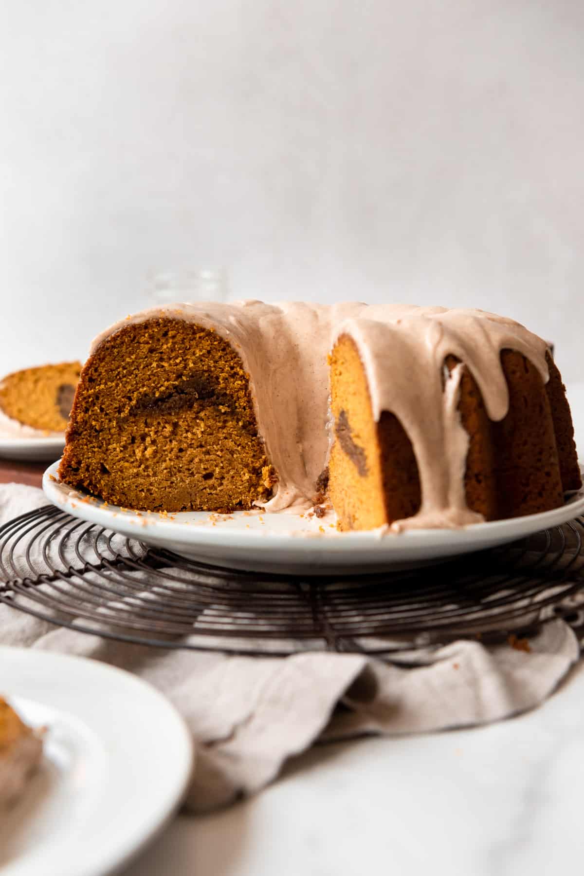 Pumpkin bundt cake is cut, revealing a brown sugar swirl inside. Servings on white plates are visible in the foreground and background. 