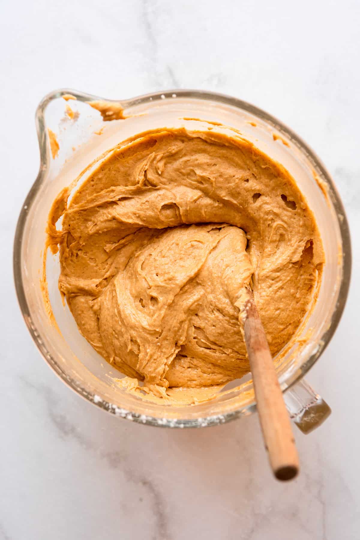 Ingredients for a spiced pumpkin bundt cake are well mixed. A wooden spoon is visible resting in the batter. 