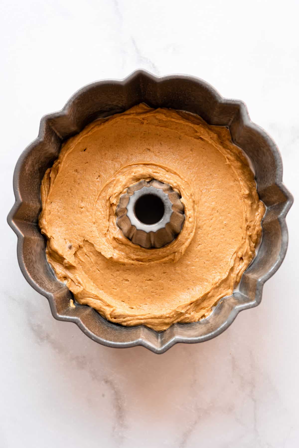 The first layer of pumpkin cake batter is placed in the bottom of a bundt pan. 