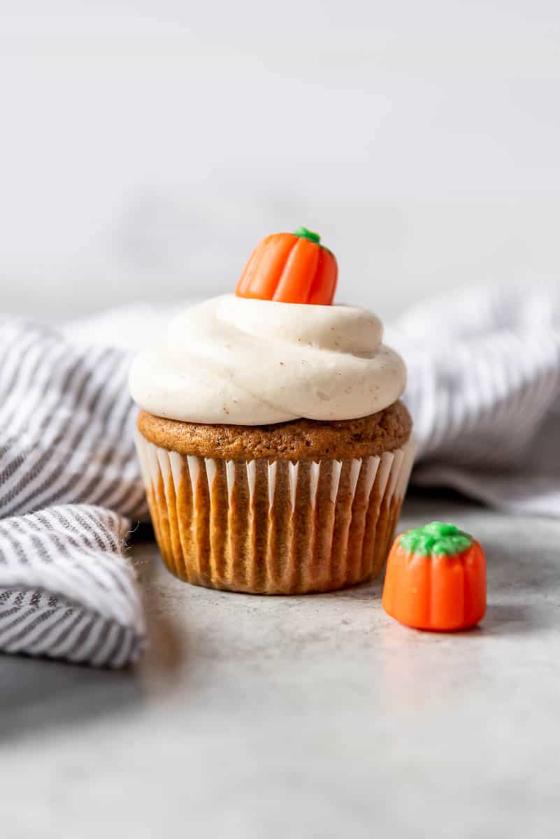 a pumpkin cupcake with cinnamon cream cheese frosting next to a striped linen napkin.