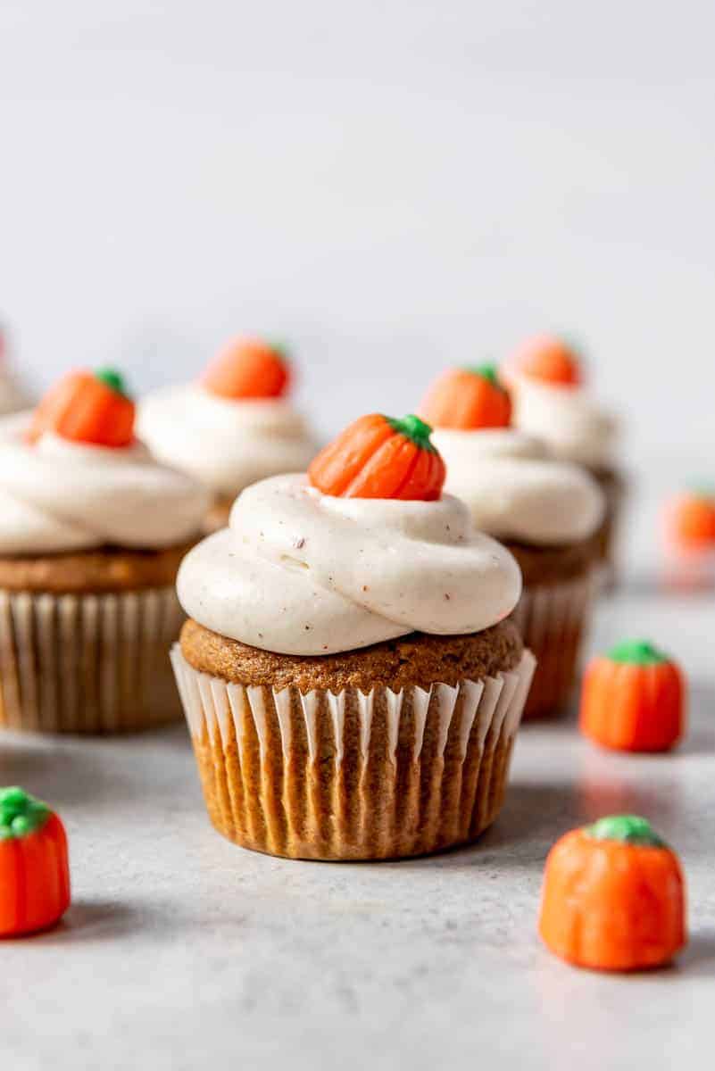 rows of pumpkin cupcakes baked in white paper liners next to candy pumpkins.