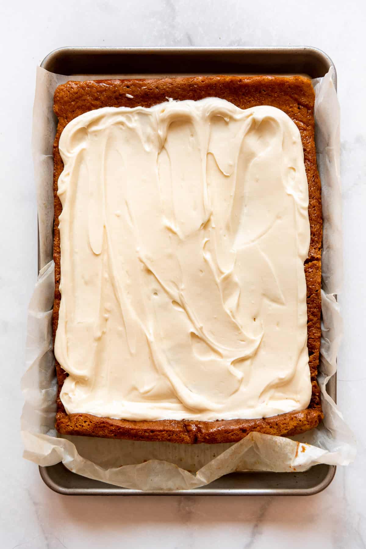 A pumpkin roll has been frosted with cream cheese frosting. 