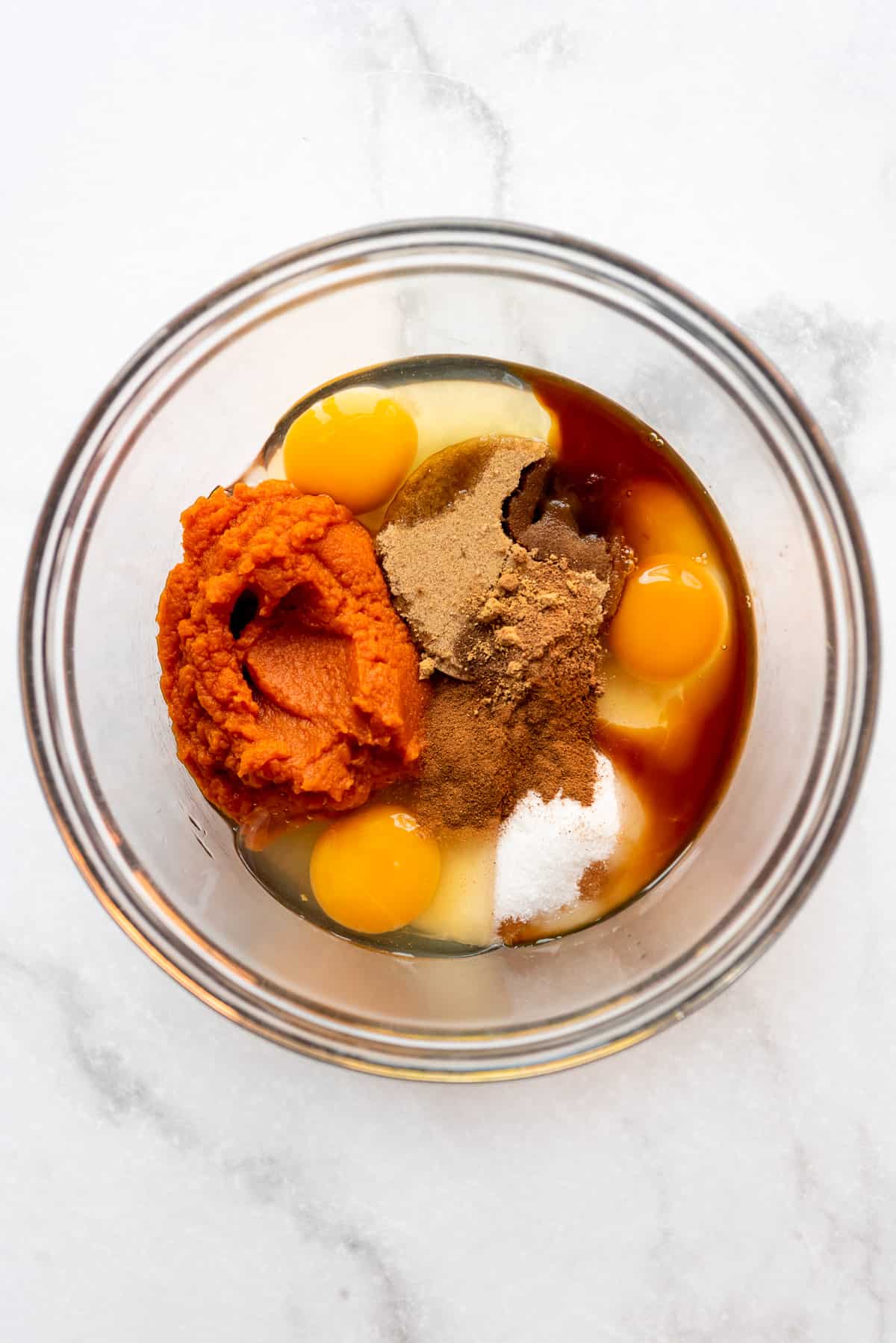 Wet ingredients for a pumpkin roll are added to a clear glass bowl. 