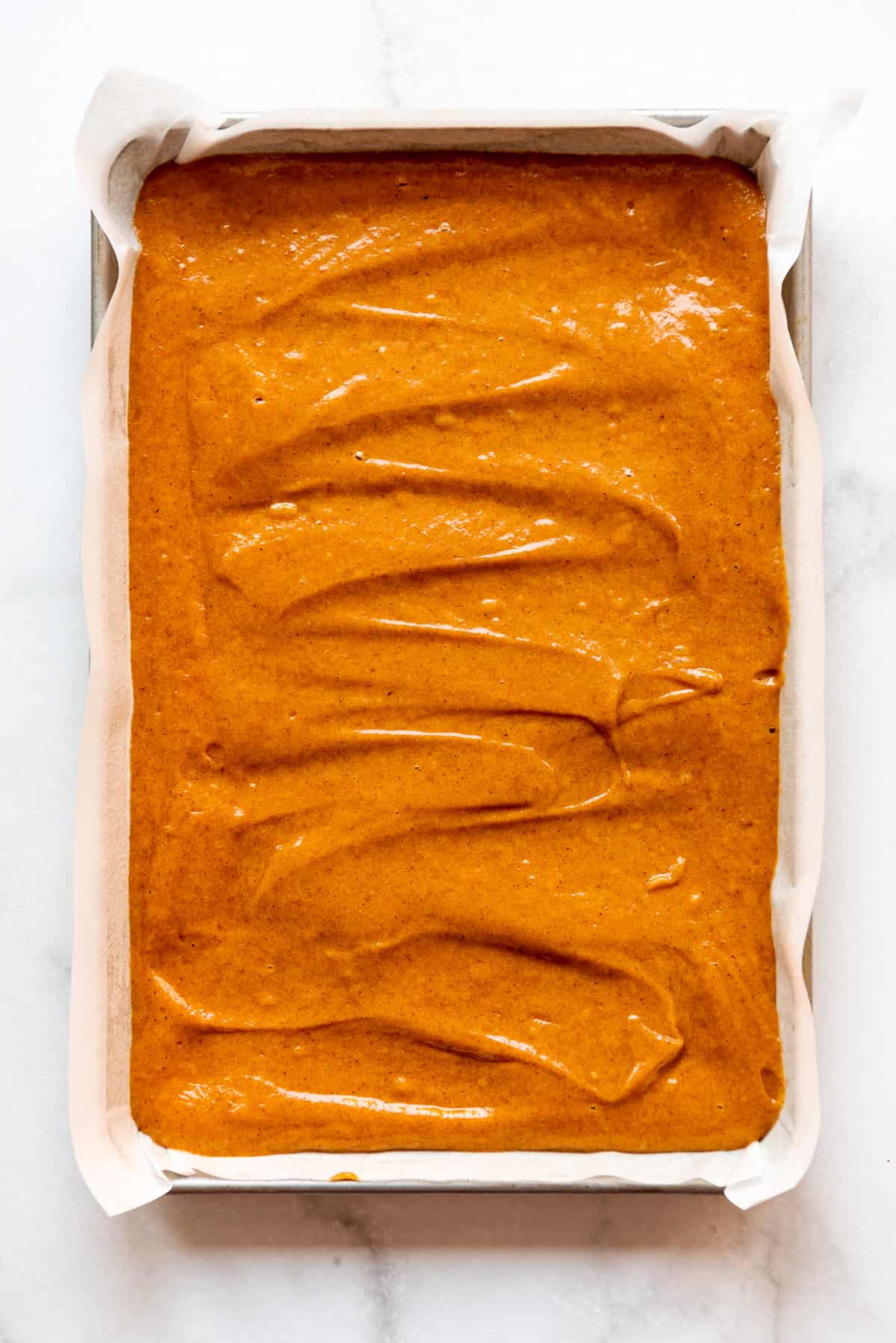 Pumpkin roll batter has been added and spread out in a jelly roll pan. 